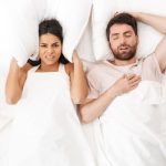 girl put pillow on ears while man snoring in sleep