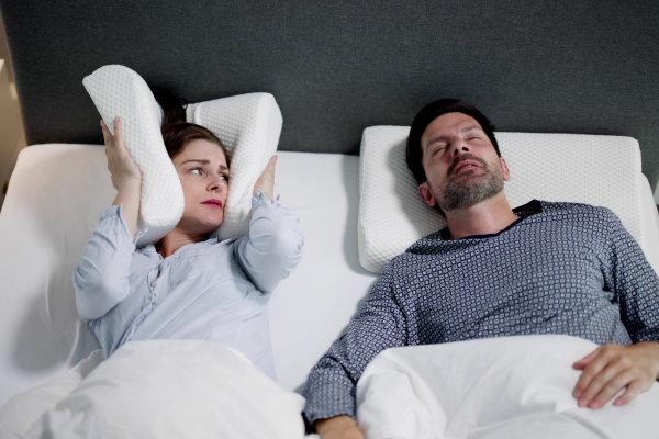 wife putting pillow on ears while man snoring in deep sleep