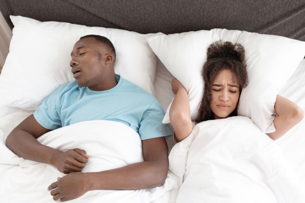 husband snoring while wife putting pillow on ear